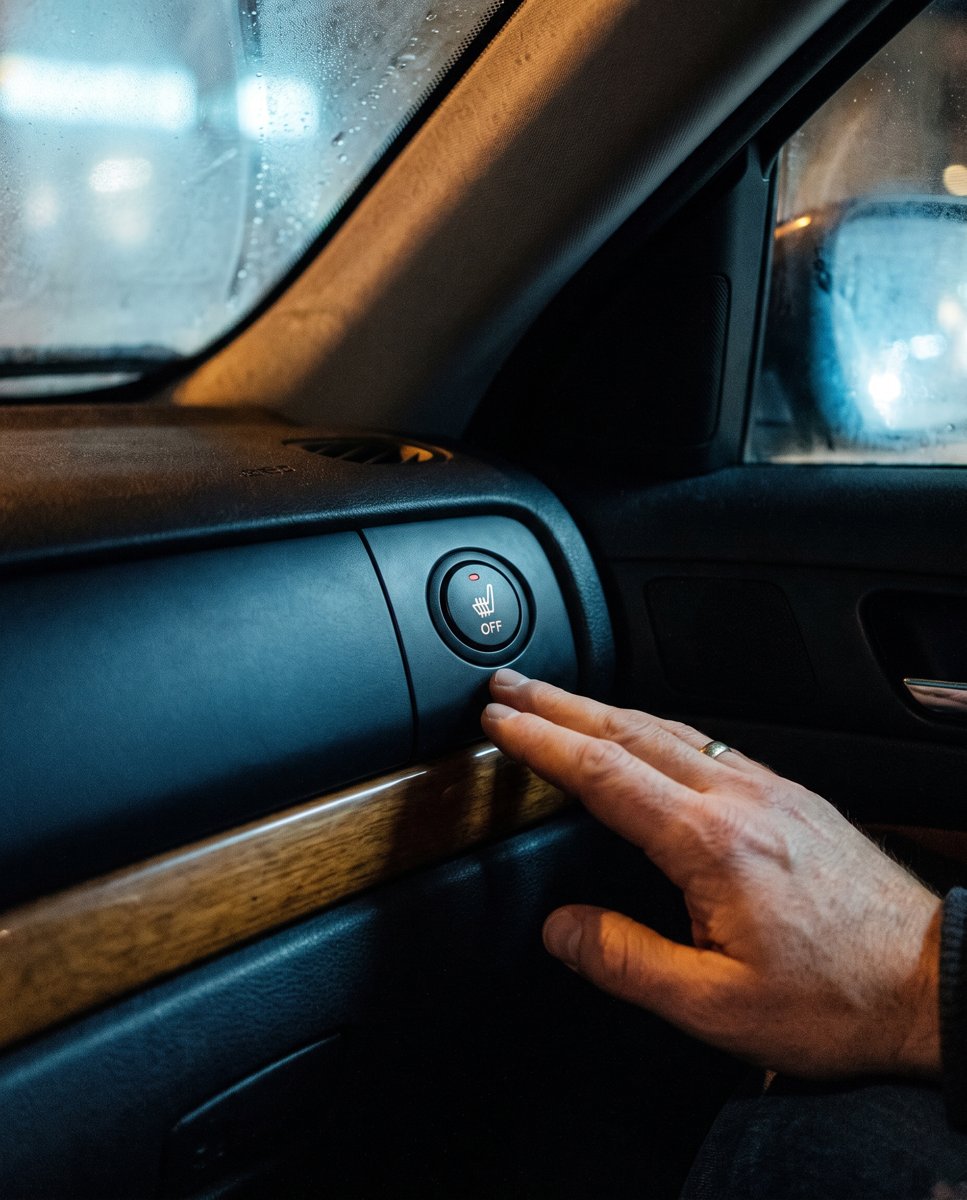 A hand by a switched-off seat heater button in a car - heat off, before the cold